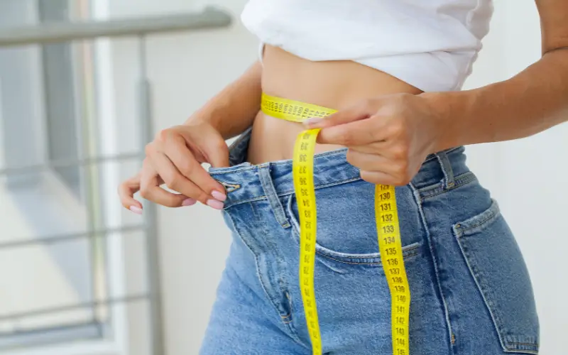Woman measuring her waist with a yellow measuring tape